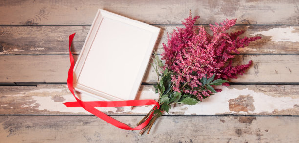 一束美丽的红色和粉红色的落新妇花，红色的丝带和空的白色框架，在古老的木制背景图片下载