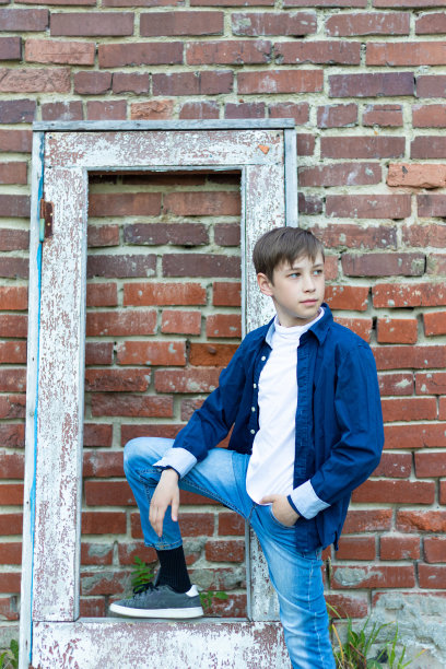 一个穿着蓝色衬衫的时髦小伙，靠着砖墙，站在一扇破旧的门旁边。特写镜头。有选择性的重点图片下载