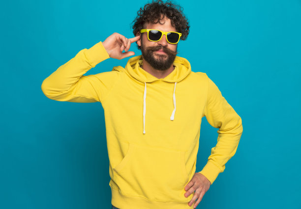 穿着黄色连帽衫的快乐年轻人手指着耳朵微笑着图片下载