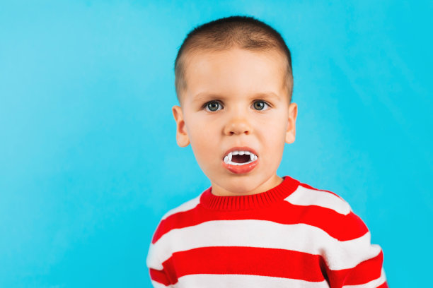 一个三岁的男孩，嘴里叼着吸血鬼的牙齿，穿着红色条纹毛衣。狂欢，假日，健康理念。图片下载