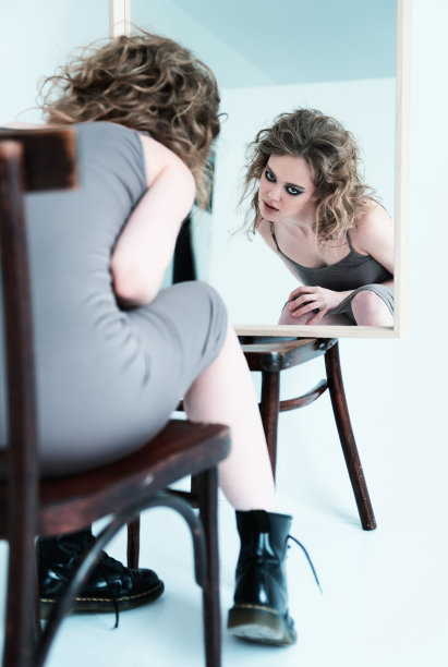 奇怪怪异的女孩的肖像。漂亮的奇怪的年轻女人坐在椅子上对着镜子图片下载