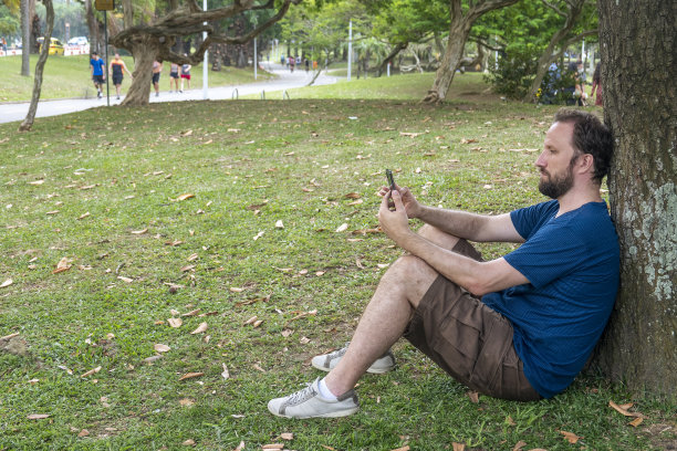 一个男人坐在公园里靠在树上发信息图片下载