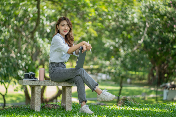 穿着休闲装的美女在国家公园背景下使用平板电脑。图片下载