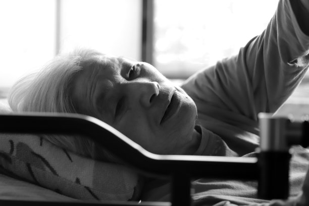 特写一位老年痴呆症妇女试图抓住东西，而她躺在护理床上图片下载