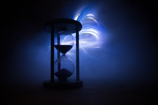 时间的概念。沙漏时钟的剪影和古老的老式木钟与箭和烟在黑暗的背景与热黄橙红蓝冷背灯，或复制空间的时间符号图片下载