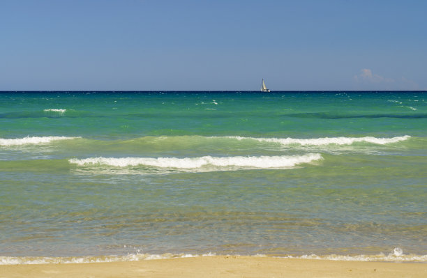 空荡荡的沙滩上有沙子，有海浪在看，有帆船在地平线上航行图片下载