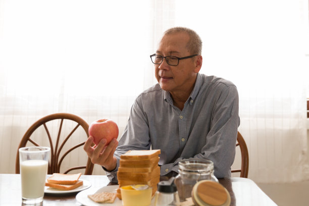 亚洲老人在家里的厨房里小心翼翼地用面包、牛奶和水果做早餐图片下载