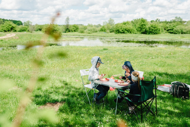 孩子们坐在桌子旁，在野餐时微笑。孩子们在湖边的自然环境中吃饭和野餐。图片下载