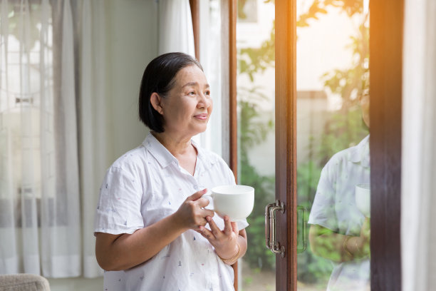 年长的亚洲妇女在家里的窗户边喝茶或喝咖啡。退休、保健和老龄化的概念图片下载