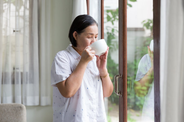 年长的亚洲女性在家中窗边喝茶或咖啡，退休、健康护理和老龄化概念图片下载