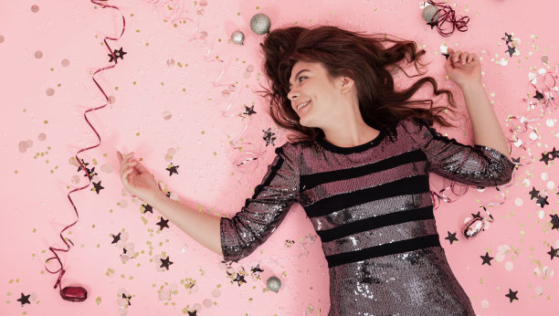 一个快乐的女孩躺在粉红色的背景下，在五彩纸屑和蛇纹石之间，俯视图。图片下载