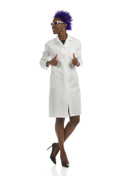 身穿白大褂的黑人女子双腿交叉站在那里，竖起大拇指，看向一边。完整的长度,孤立。图片下载