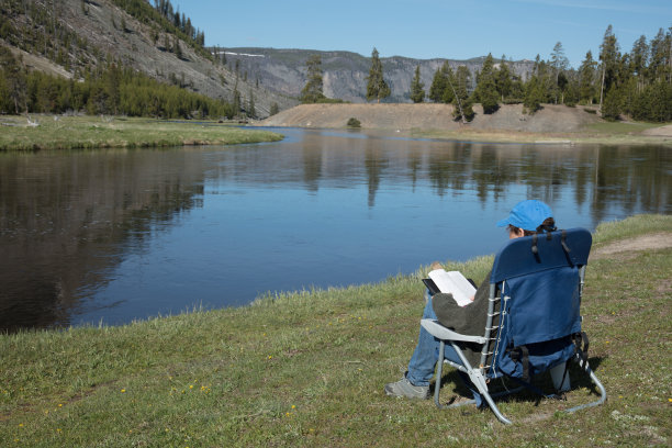 在黄石国家公园的一条山河边，一个人坐在矮椅上看书图片下载