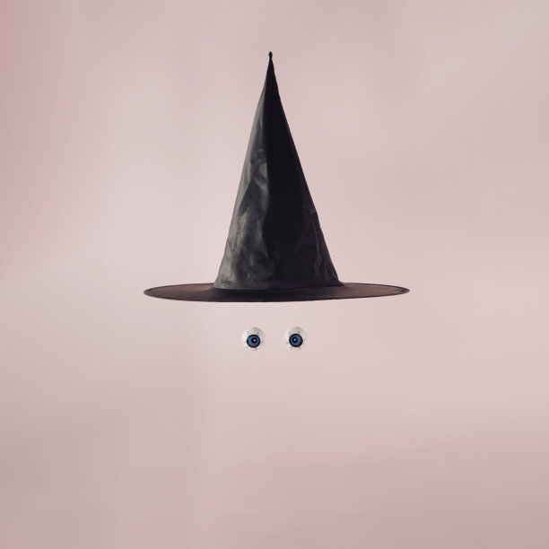 黑色万圣节女巫帽，两个蓝色的眼睛漂浮在淡粉色的背景上。万圣节庆祝活动的概念。图片下载