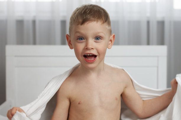 一个齐腰高的小男孩裹着白色的毯子微笑着图片下载