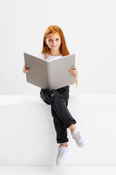 小白种人学前班女孩的肖像与书的姿势孤立在白色的工作室背景。图片下载