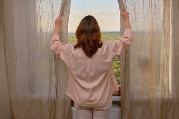 一个身穿粉红色衬衫的女人站在窗前拉开窗帘图片下载