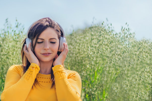 一名身穿黄色衣服的年轻女子在绿色背景下戴着耳机，闭着眼睛听音乐。图片下载