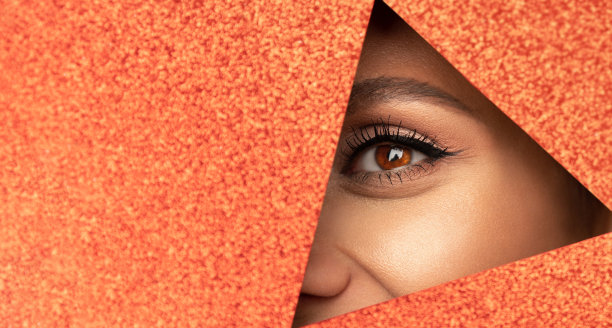 一张年轻美丽的女孩的脸，画着明亮的妆，丰满的红唇从亮闪闪的红纸上的一个洞里窥视着。图片下载