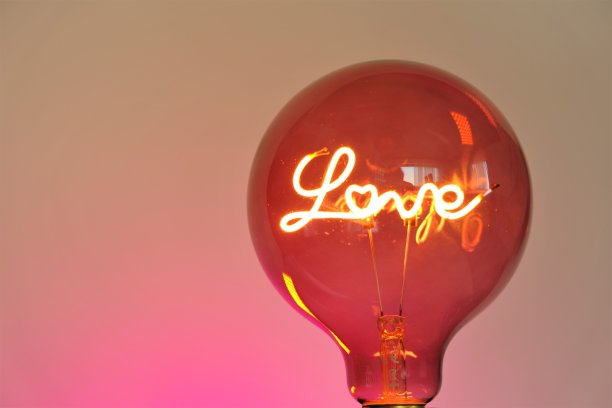 情人节。爱的象征。粉红色背景上刻有“爱”字样的灯泡。节日浪漫的背景。爱情和关系的象征。图片下载