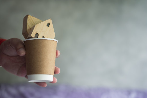 手拿一次性棕色纸杯与木头家的特写。家庭护理。Home for sale概念。图片下载