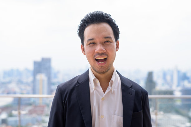 快乐的亚洲商人穿着西装在城市的屋顶笑图片下载