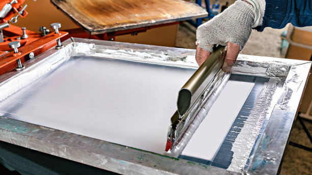 绢网印花印刷生产。丝印纺织品。男性手拿橡皮擦。手工丝网印刷设计工作室图片下载