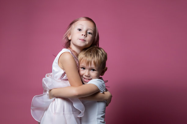 白种兄妹，在粉红背景的摄影棚里拥抱。图片下载