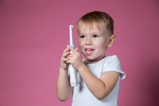 一个微笑的白人小男孩拿着粉红色背景上的电动声波牙刷图片下载