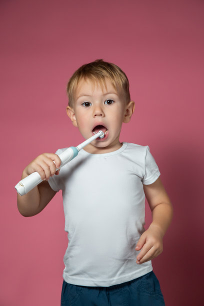 一个微笑的白人小男孩正在用电动声波牙刷刷牙图片下载