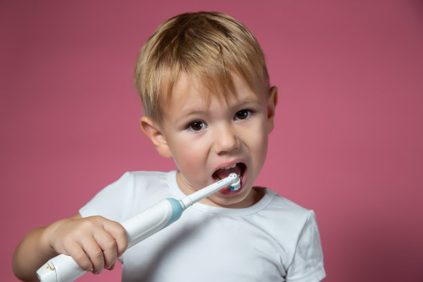 一个微笑的白人小男孩正在用电动声波牙刷刷牙图片下载