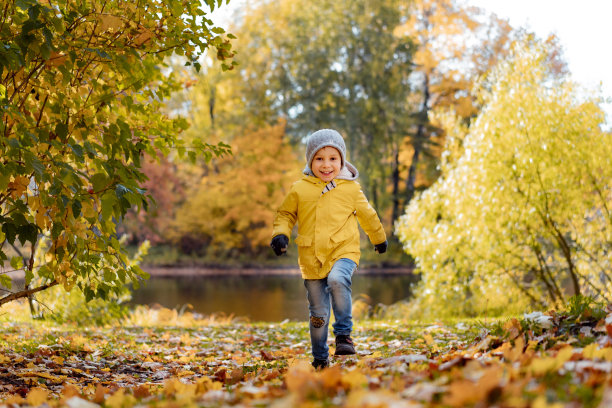 在十月阳光明媚的日子里，一个穿着黄色夹克的快乐小男孩在俄罗斯圣彼得堡的秋天中央公园跑步图片下载