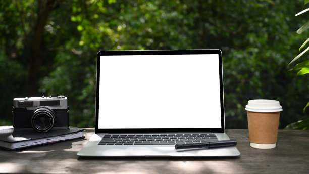 在绿色花园的木桌上模拟笔记本电脑，咖啡杯和复古相机。图片下载