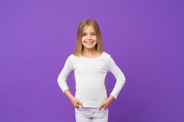 孩子穿着白色套头衫和牛仔裤，青年时尚概念。长着金色长发的女孩。可爱的孩子，大大的微笑孤立在紫色的背景上。有着可爱脸庞和淡褐色眼睛的女学生图片下载