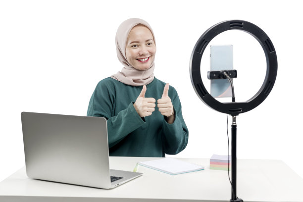 亚洲穆斯林妇女用笔记本电脑和带有照明设备的手机制作视频博客图片下载