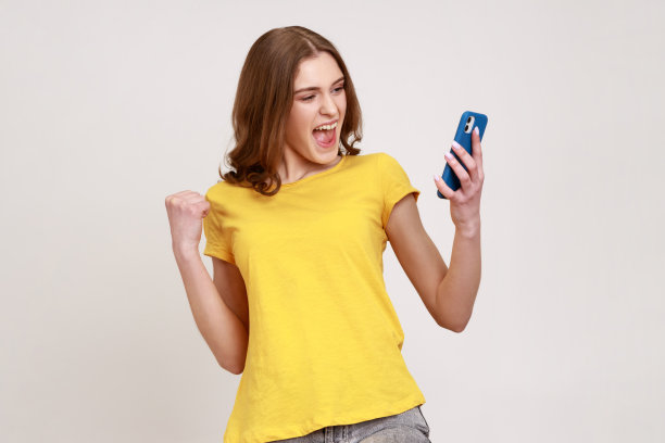 照片中的少女欣喜若狂，穿着t恤欢呼雀跃，手里拿着手机，紧握拳头，成功地在网上赚钱。图片下载