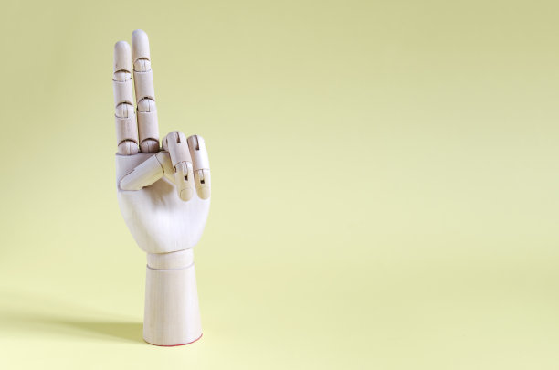 黄色背景上伸出两只手指的木手。概念手势木手伸出两根手指。图片下载