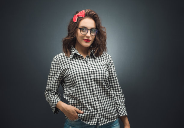 复古风格的女士，双手插在口袋里，站在深灰黑色的背景下看着镜头。有吸引力的女孩。图片下载