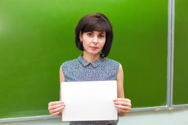 在学校教室里，一位老师拿着一张白纸站在黑板前图片下载