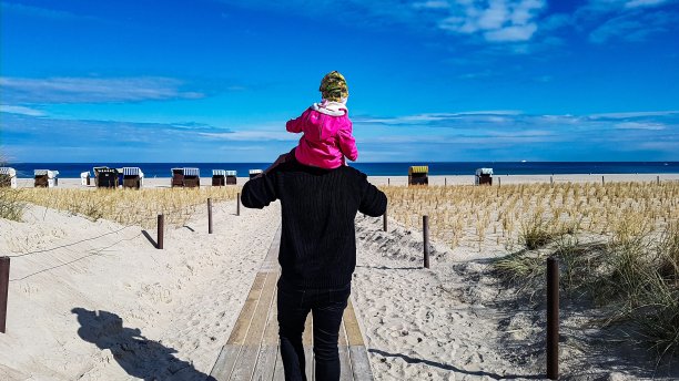 让父亲和孩子骑在他们的肩膀上在海滩上散步图片下载