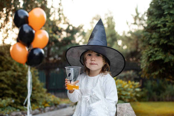 可爱的女孩戴着女巫帽在万圣节派对上喝果汁图片下载