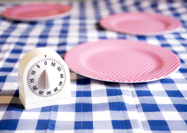 厨房计时器放在蓝色格子布的桌子上。红色检查空车牌的背景图片下载