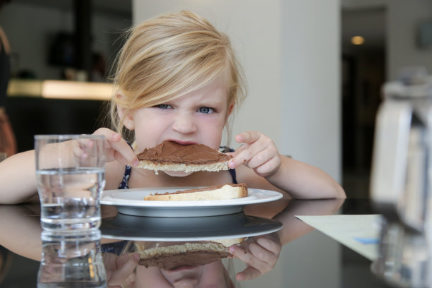 小女孩早餐吃着面包上的巧克力奶油。图片下载