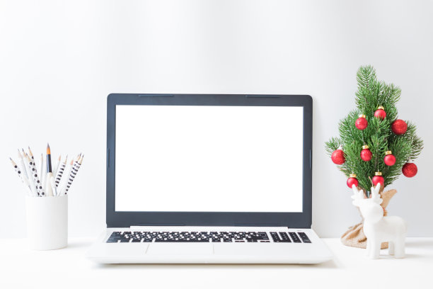 办公空间与笔记本电脑模型屏幕，圣诞树，鹿，用品在一个明亮的背景。圣诞家庭内部或办公室背景图片下载