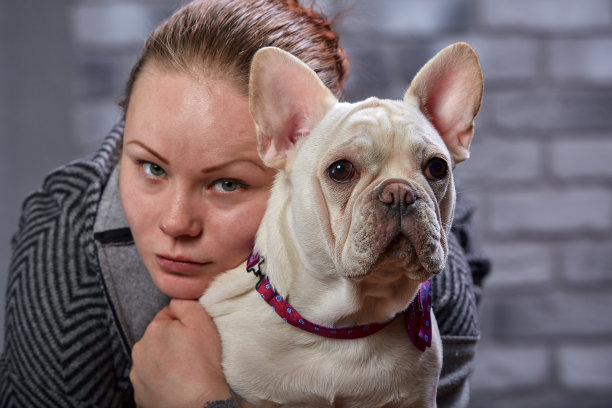 年轻美丽的女人拥抱她的法国斗牛犬小狗并亲吻他-爱情，友谊的概念图片下载