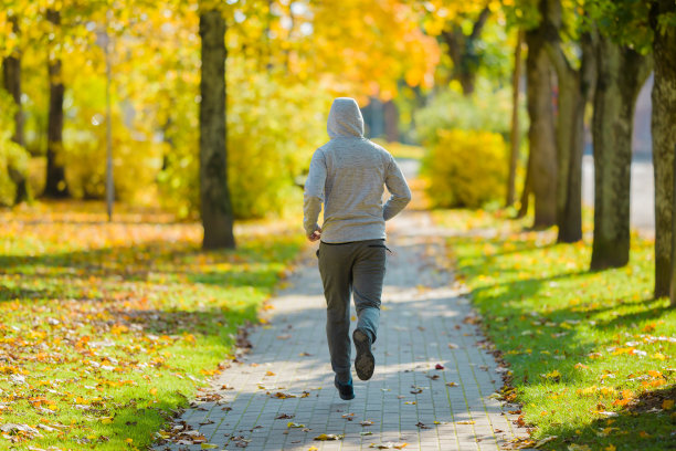 一个年轻的成年人在城市公园的人行道上跑步。每日活跃的生活方式。后视图。图片下载