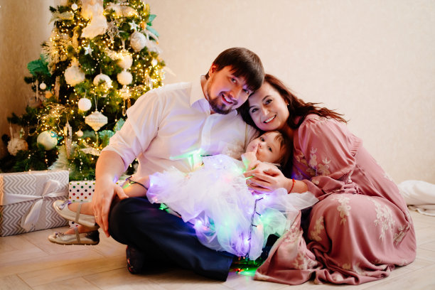 爸爸、妈妈和小女儿在圣诞树旁玩花环。图片下载