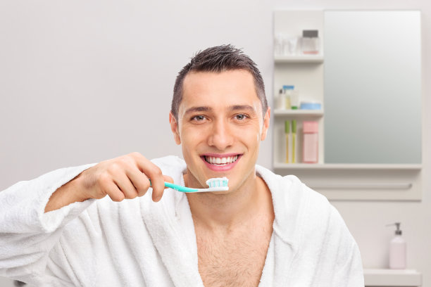 浴室里，一个微笑的男人拿着牙刷和牙膏图片下载