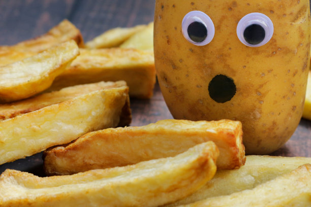 全帧图像的生宝宝新土豆周围的油炸薯片木纹背景，画上的嘴和瞪大的眼睛添加到土豆给一个担心，恐怖的外观，幽默的概念，聚焦前景图片下载