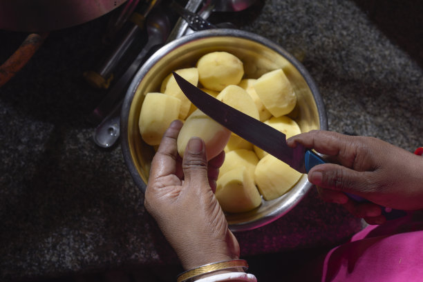 母亲用刀在银锅里把生土豆切成两半。厨房侧面特写照片图片下载